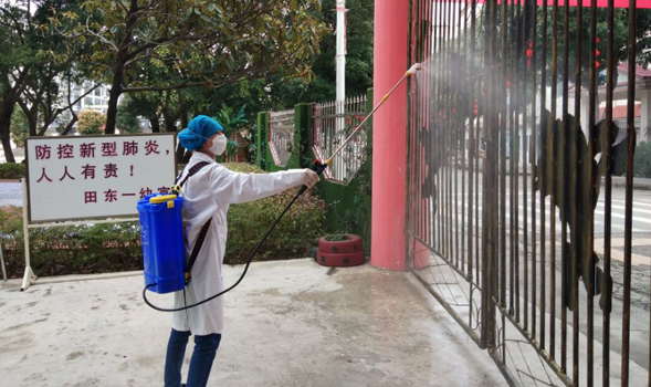 Une jeune femme portant un équipement de protection complet asperge de solution désinfectante un portail en fer fermé.