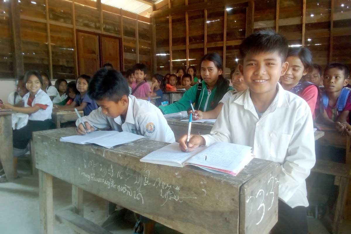 Au Laos, un garçon sourit tout en travaillant sur son bureau dans une salle de classe. Il écrit dans un carnet.