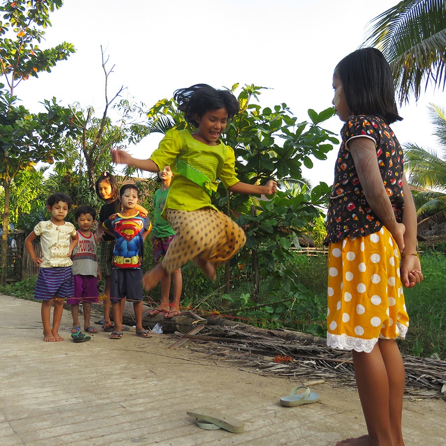 Une fille saute en jouant dans la rue avec d’autres enfants.