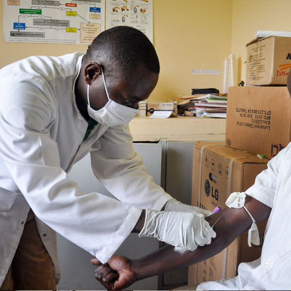 Un travailleur médical portant un masque et des gants utilise une seringue pour prélever du sang d’un bras tendu.