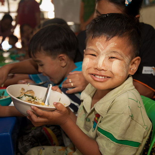 Un garçon, parrainé par Vision Mondiale, souriant en tenant un bol de nourriture..