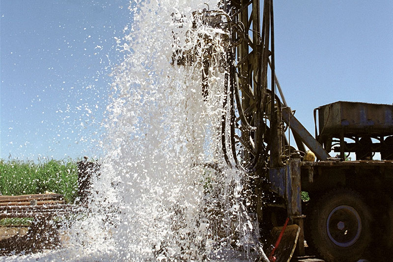 Water gushes out of the ground after a heavy machine finishes drilling for a well.