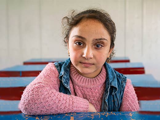 Malak, 8 ans, assise devant son pupitre à Mossoul, en Irak. Lors d’une fusillade, Malak est devenue aveugle de l’œil gauche. Elle en garde aujourd’hui la cicatrice