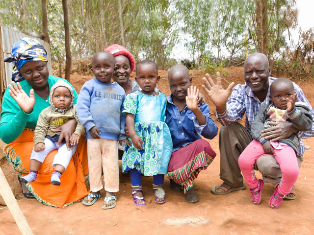 Devant leur foyer, une famille souriante de huit personnes salue le photographe.