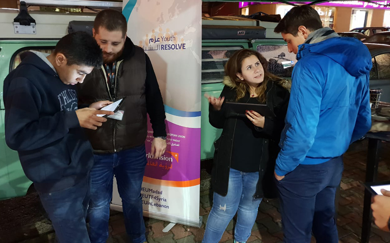 Four young people standing in pairs chatting about what they see on electronic tablets.