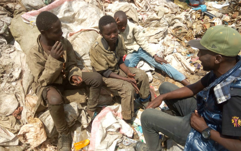 Un groupe de quatre jeunes hommes assis sur une pile d’ordures