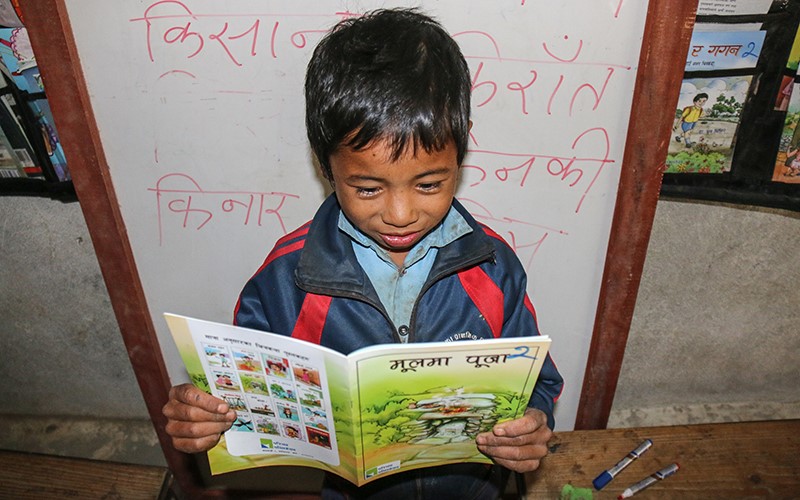Milan, un jeune garçon, tient un livre dans ses mains pendant qu’il en fait la lecture.