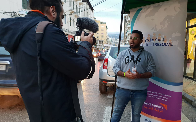 A young man uses a camera to film another young man, who is doing a stand up.