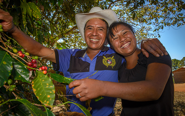 Un père et une fille honduriens s’enlacent en riant et en regardant l’objectif. Ils tiennent dans leur main un plant de café qu’ils récolteront bientôt.