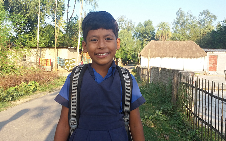 A young girl living in Bangladesh is walking to school wearing her blue school uniform and backpack.