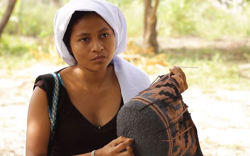 A Colombian woman gestures to a bag she is weaving