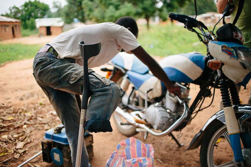 A young man that has suffered a permanent injury to his right leg is working fixing a motorcycle.