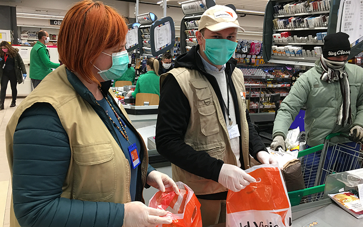 Une femme et un homme portant des masques protecteurs et des gants aident à emballer des articles dans un supermarché