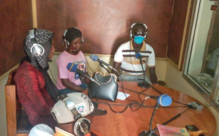 Trois personnes sont assises devant des micros, autour d’une table, dans un studio de radio