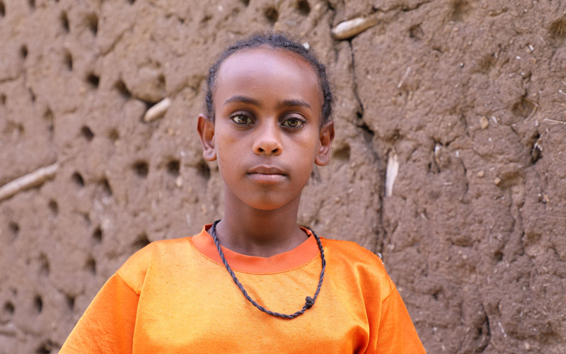Une jeune fille éthiopienne se tient devant un mur en terre