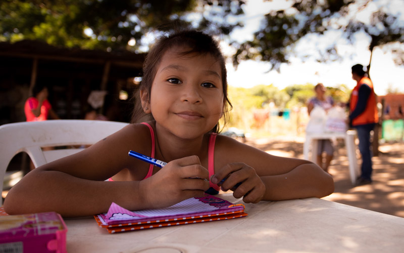 Une fillette bolivienne est assise à un bureau avec carnet et sourit.