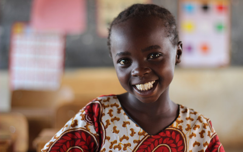 Une fillette kenyane est assise dans une classe et sourit à l’objectif.