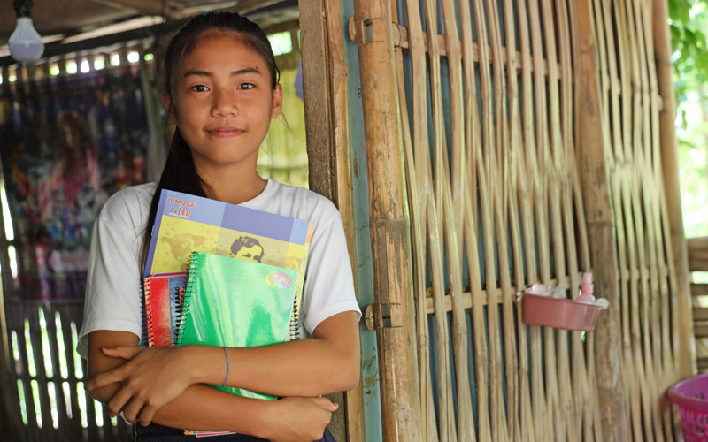 Une jeune fille des Philippines tient des livres, debout devant une entrée.