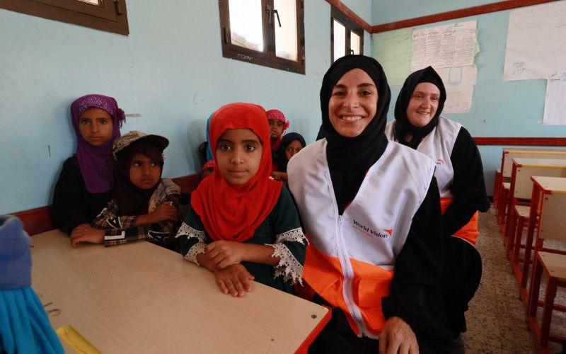 Children and World Vision staff smile in a classroom.