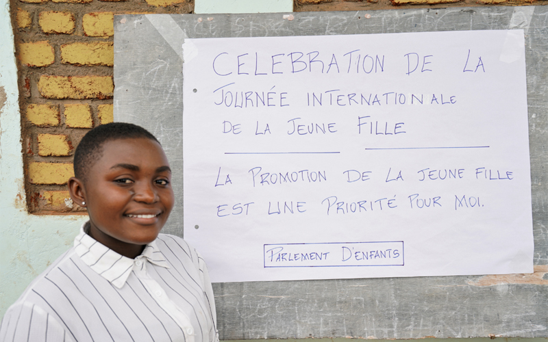 Une jeune fille congolaise se tient devant un mur de briques.