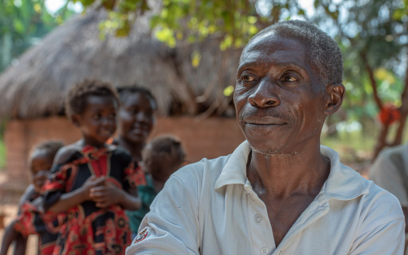 father looks on while children play in the background.