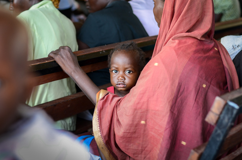 A mother sitting on a bench with her baby on her lap.