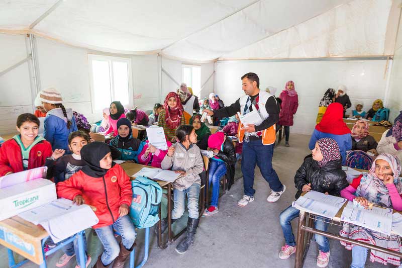 Les enfants réfugiés syriens sont assis aux pupitres de l'école dans une salle de classe installée dans une tente du camp de réfugiés.
