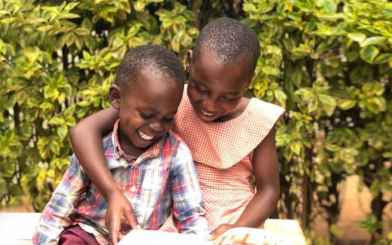 Une fille lisant joyeusement un livre à un garçon plus jeune.