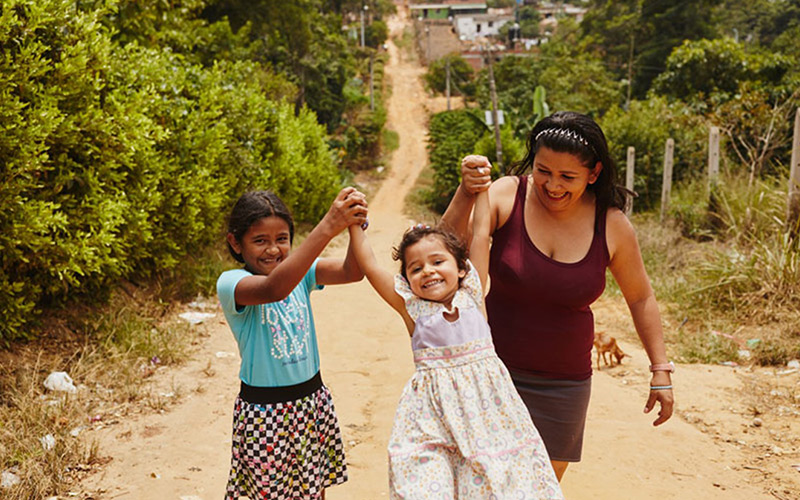 Une femme et deux enfants rient et se tiennent la main en parcourant un chemin de terre.