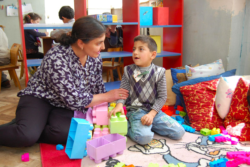 Une femme est assise à côté d’un jeune garçon dans un centre d’apprentissage. Elle l’aide pendant qu’il joue.