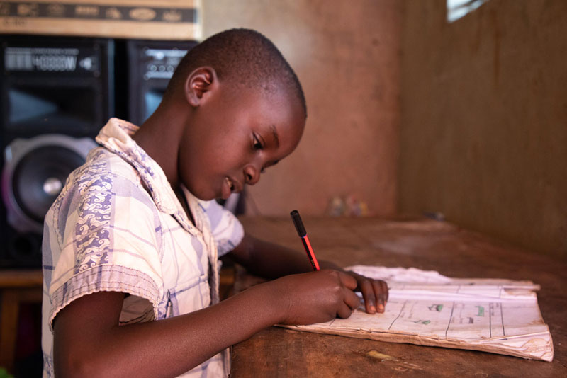 Un enfant assis à un bureau, écrivant dans un cahier.