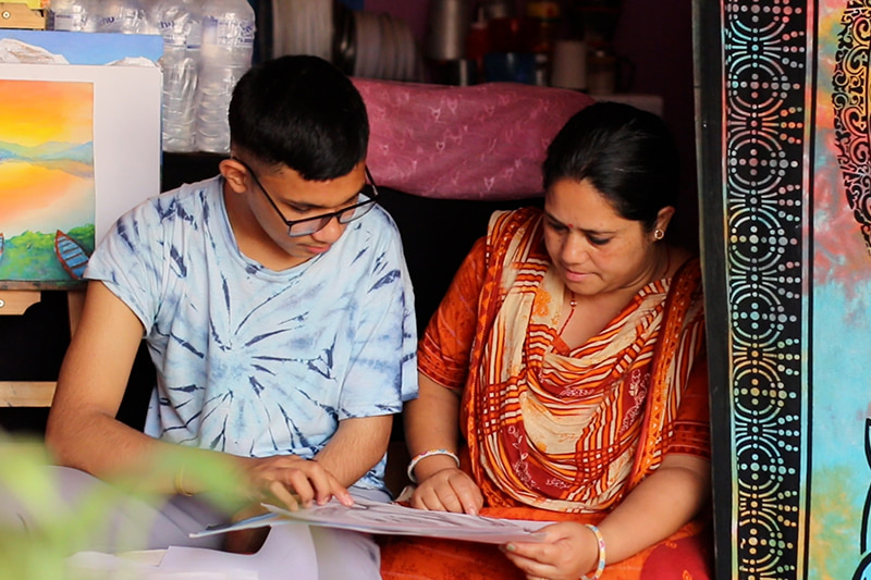 Rahul et sa mère assis côte à côte, regardant l’un de ses dessins.