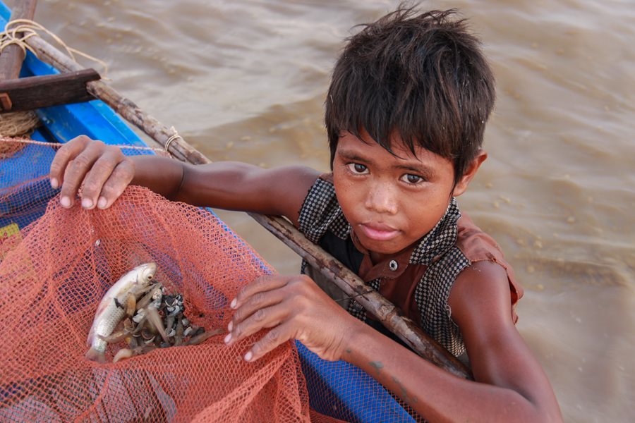 Un enfant travailleur dans l'eau tenant un filet contenant du poisson sur le bord d'un bateau.
